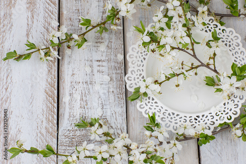 On a white wooden background  a white plate and a branch of cherry blossoms.