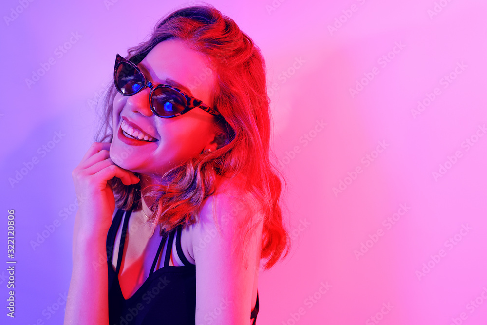 Beautiful girl in neon. Fashion photo of a short-haired girl, dancing, sun glasses. Girl in red and blue light posing. Happy girl smiles, laughs, good emotions.