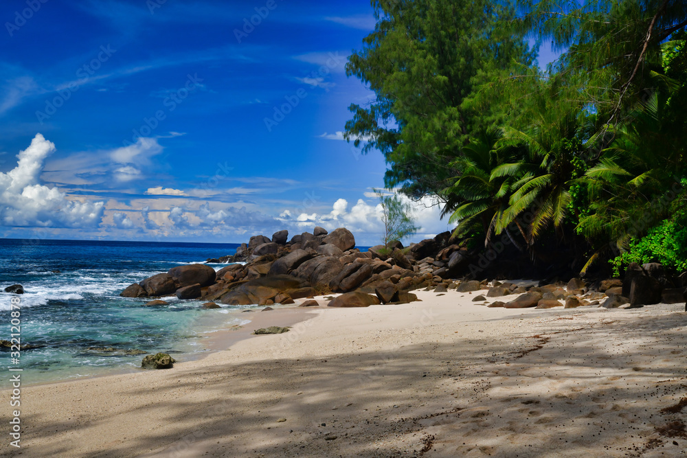 Ocean waves and granite rocks - Takamaka beach, Mahe Island, Seychelles. Palmtrees, sand, crashing waves, beautiful shore, blue sky and turquoise water.