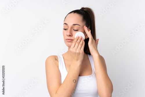 Young brunette woman over isolated white background with cotton pad for removing makeup from her face