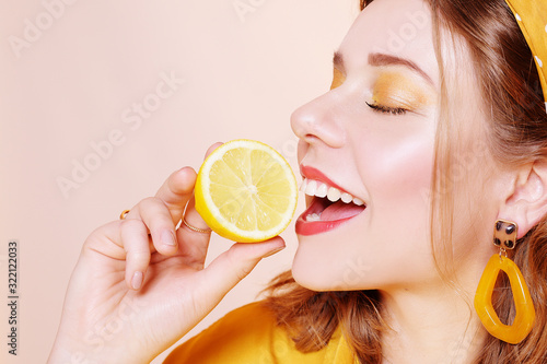 A beautiful portrait of a girl who eats a lemon, bites off a slice of lemon, a girl sniffs a lemon. Health, skin beauty, lemon-based face masks, lemon diet. Girl with bright  make-up.