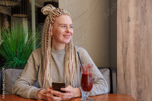 Smiling hipster woman kanekalons drinking berry cocktail smoothie and use smartphone photo