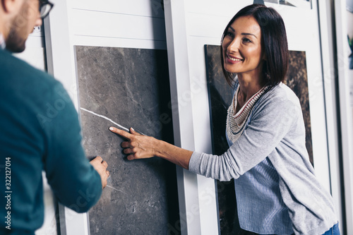 Middle age man choosing ceramic tiles and utensils for his home bathroom and female seller helps him to make right decision
