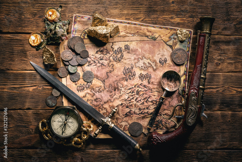 Pirate treasure map and other accessories on brown wooden table flat lay background.
