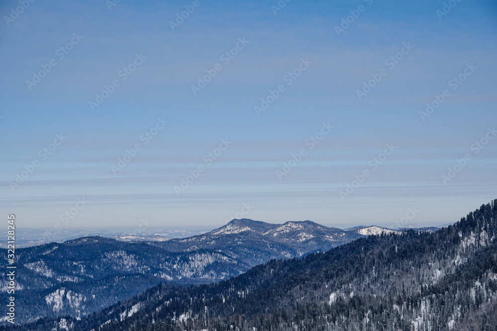 Obraz premium Winter mountain landscape. Snowy mountains overgrown with taiga against a background of gray clouds and blue sky. Russia. Siberia. Altai Republic.