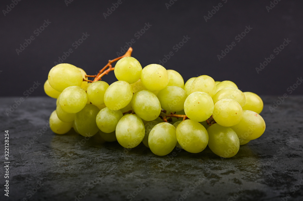 A bunch of green grape on a marble dark background. Volumetric winery. A bunch of green grape bush. A bunch of green grape on a marble dark background. Volumetric winery. A bunch of green grape bush.