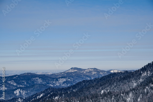 Winter mountain landscape. Snowy mountains overgrown with taiga against a background of gray clouds and blue sky. Russia. Siberia. Altai Republic.