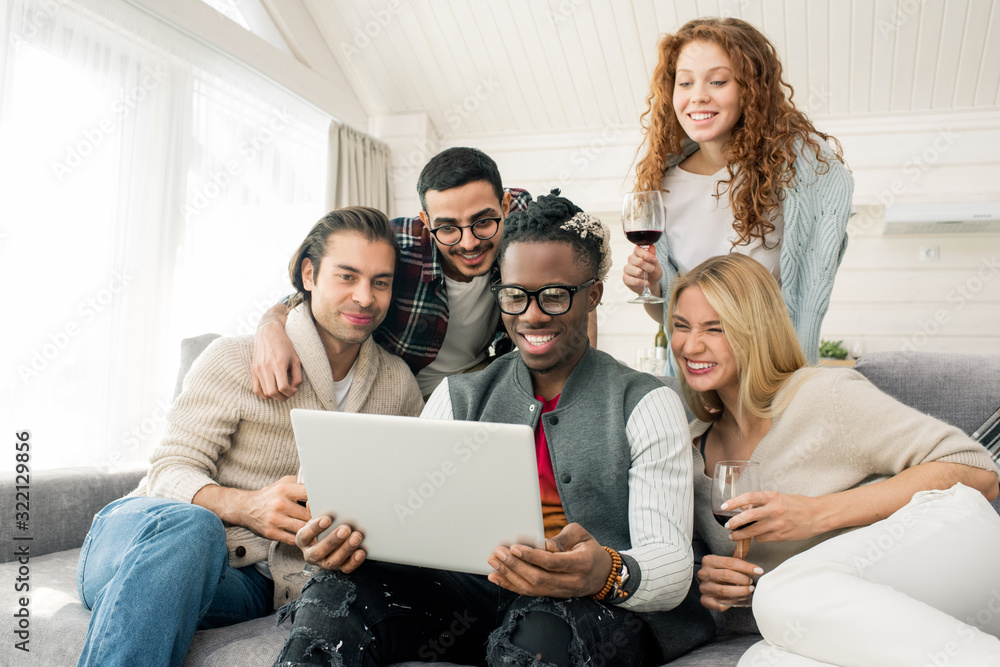 Group of cheerful multi-ethnic friends having fun looking at photos on laptop together, horizontal shot Group of cheerful multi-ethnic friends having fun looking at photos on laptop together, horizontal shot
