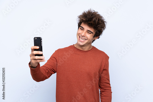 Young caucasian man over isolated blue background making a selfie