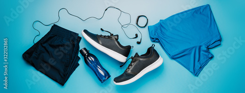 Flatlay blue clothing for running or crossfit, headphones, fitness bracelet, water bottle, shorts and t-shirt on a blue background