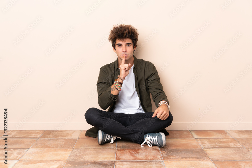 Young caucasian man sitting on the floor showing a sign of silence gesture putting finger in mouth Young caucasian man sitting on the floor showing a sign of silence gesture putting finger in mouth