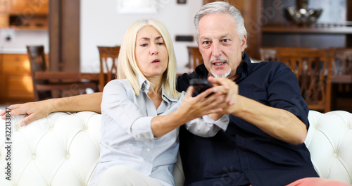 Mature couple fighting for remote control on a sofa
