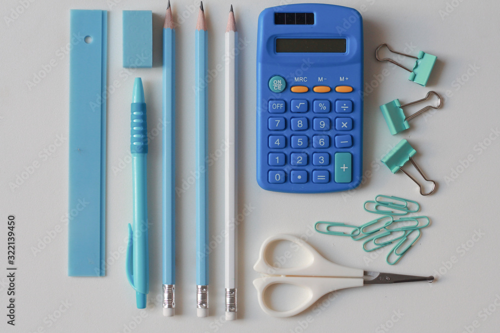 Stationary school supplies in white and blue tone, Scissors, pencils, paper clips,calculator, notepad on blue and white background, Flat lay. Stationary school supplies in white and blue tone, Scissors, pencils, paper clips,calculator, notepad on blue and white background, Flat lay.