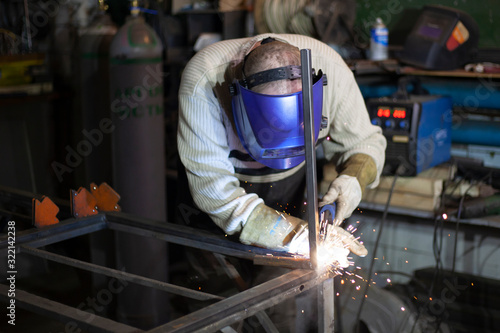 Welder at work. The welder heats the metal. Classes in the workshop. Steel processing. Welder in a blue welding mask. High melting point of metal. A man doing hard work.