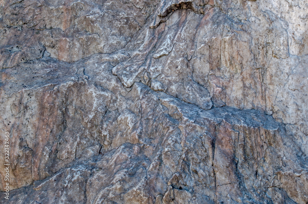 Texture of a large solid stone with a relief gray-brown pattern with chips and protrusions, veins and swellings. Natural organic background for design