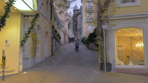 Calle solitaria de ciudad con anciana subiendo cuesta cansada photo