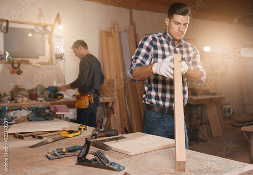 Professional carpenter and colleague working with wooden plank in workshop
