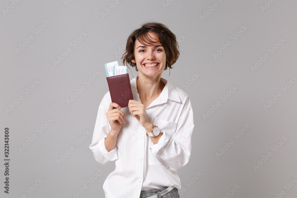 Smiling young business woman in white shirt posing isolated on grey background studio portrait. Achievement career wealth business concept. Mock up copy space. Holding passport, boarding pass, ticket. Smiling young business woman in white shirt posing isolated on grey background studio portrait. Achievement career wealth business concept. Mock up copy space. Holding passport, boarding pass, ticket.