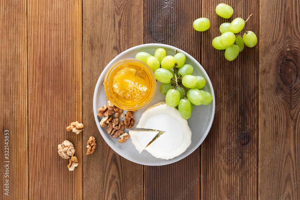 Cheese plate round sliced soft cheese with grapes and honey on wooden table, flat lay. Cheese plate round sliced soft cheese with grapes and honey on wooden table, flat lay.