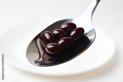Astaxanthin capsules in the spoon on a white plate background. Close-up