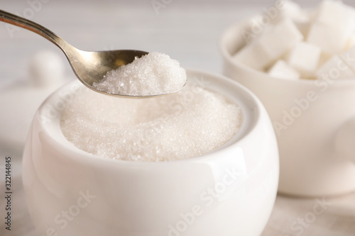 Taking spoon of white sugar from ceramic bowl on table, closeup