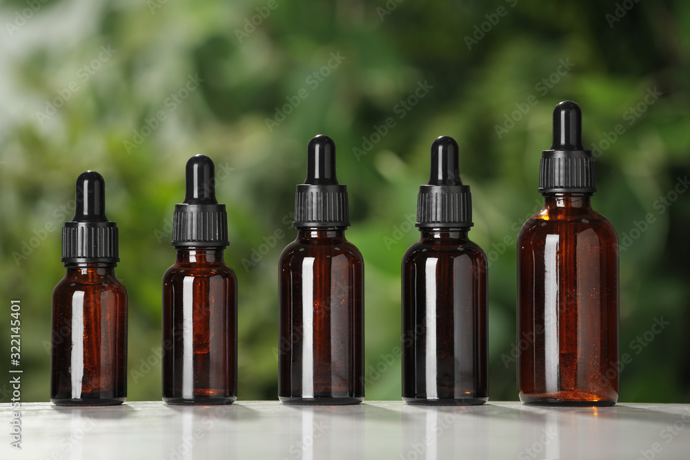Glass bottles on white table against blurred green background Glass bottles on white table against blurred green background