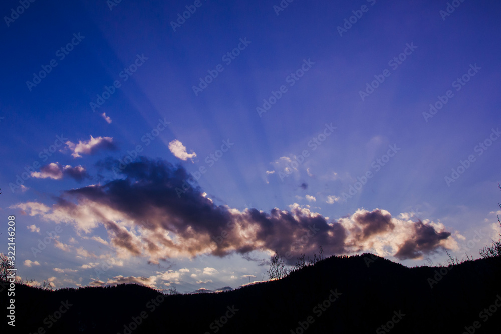Beautiful clouds against blue sky and silhouettes of mountain and trees, daytime in the forest, sunset in the nature