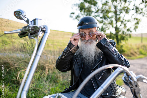 A senior man traveller with motorbike and sunglasses in countryside.