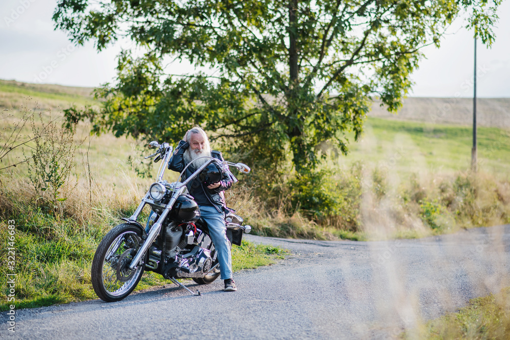 Obraz premium Starszy człowiek podróżujący z motocyklem na wsi. Skopiuj miejsce.