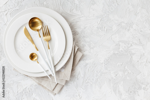 Beautiful gold and white cutlery on white plate on light white gray background