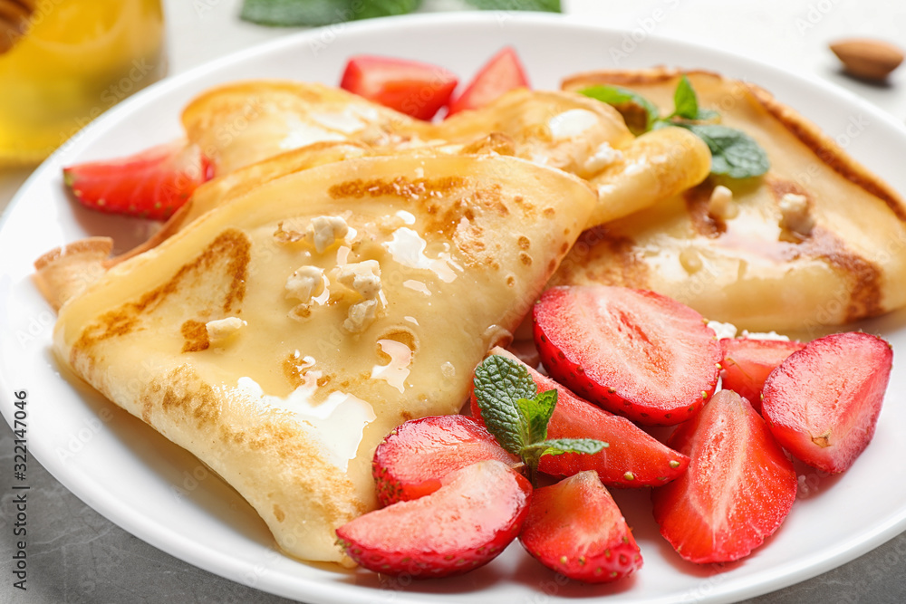 Delicious thin pancakes with strawberries, cottage cheese and honey on light table, closeup