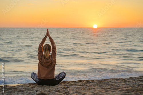 woman doing meditation on the beach; girl sitting in yoga pose on sunset and looking to the sea.