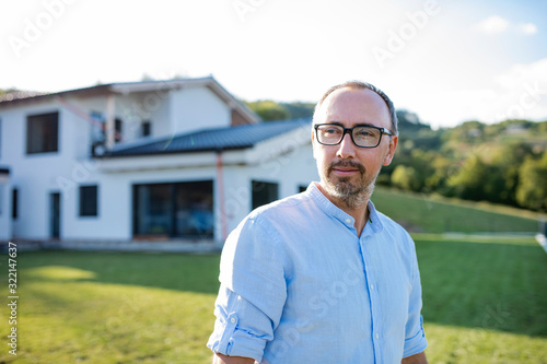 A portrait of man standing outdoors in garden by a house.