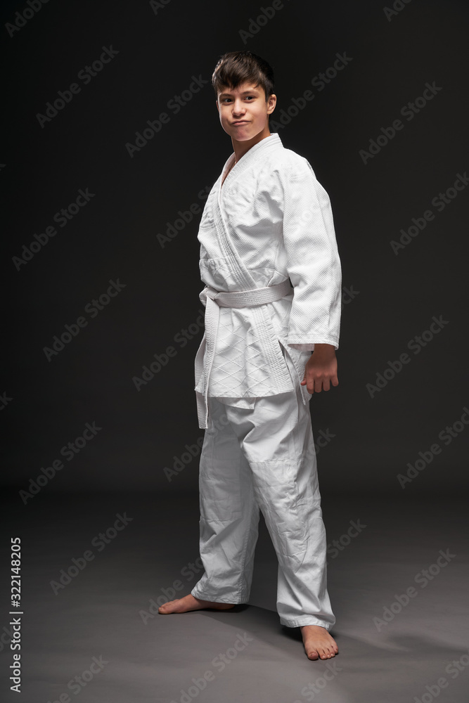 a teenager dressed in martial arts clothing poses on a dark gray background, a sports concept a teenager dressed in martial arts clothing poses on a dark gray background, a sports concept