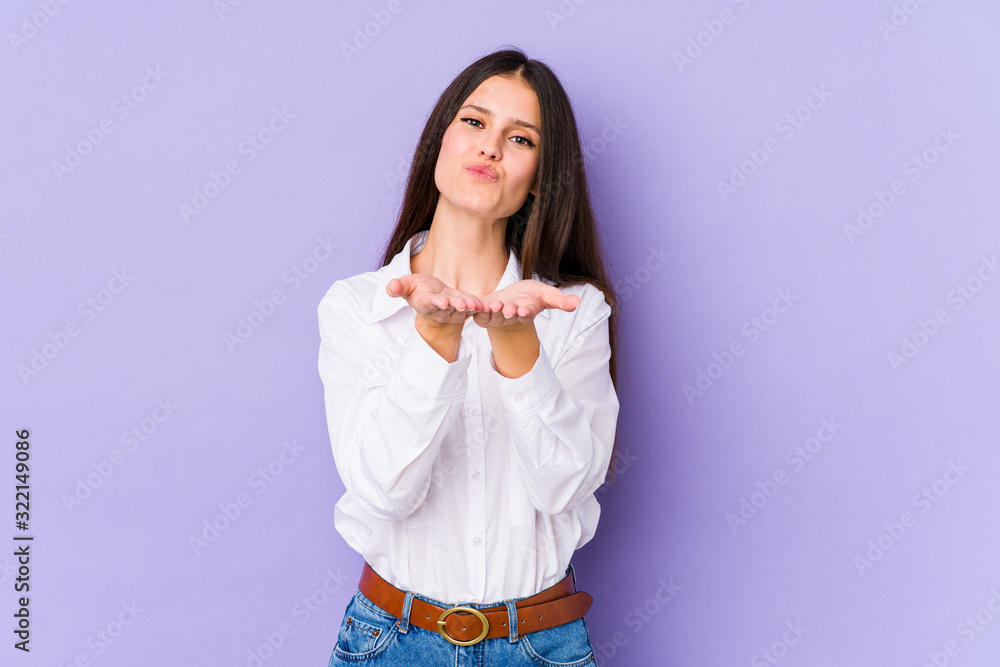 Young caucasian woman isolated on purple background folding lips and holding palms to send air kiss. Young caucasian woman isolated on purple background folding lips and holding palms to send air kiss.
