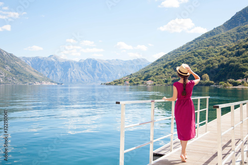 Young woman at sea beach. Rear view of graceful girl traveler in straw hat in summer vacation. Lady waiting on pier. Concept of travel, femininity, solo female tourism, holiday, adventure.