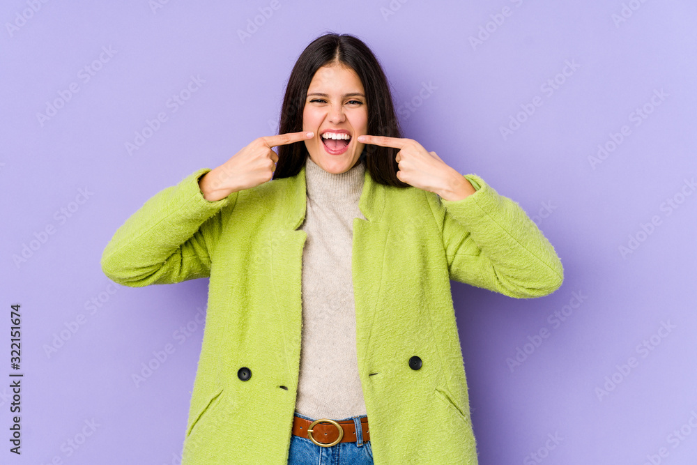Young caucasian woman isolated on purple background smiles, pointing fingers at mouth. Young caucasian woman isolated on purple background smiles, pointing fingers at mouth.