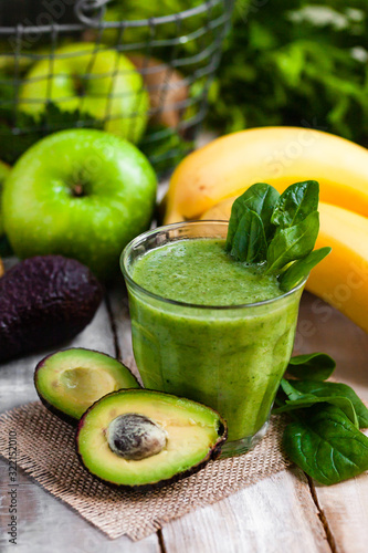 Healthy food and vegan diet concept - glass of fresh green juice or smoothie with kiwi, spinach, banana, avocado, apple. Antioxidant detox beverage with raw ingredients.  Close up, wooden background.