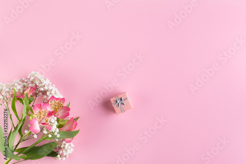 A bouquet of pink and white flowers and a small gift box on a pink paper background. © Galyna Chyzh