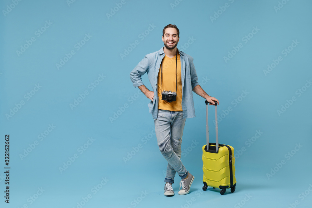 Smiling traveler tourist man in yellow summer casual clothes with photo camera isolated on blue background. Male passenger traveling abroad on weekends. Air flight journey concept. Holding suitcase. Smiling traveler tourist man in yellow summer casual clothes with photo camera isolated on blue background. Male passenger traveling abroad on weekends. Air flight journey concept. Holding suitcase.