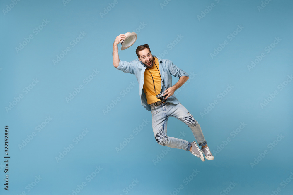 Funny traveler tourist man in yellow summer casual clothes with photo camera isolated on blue background. Male passenger traveling abroad on weekend. Air flight journey concept. Jumping, rising hat. Funny traveler tourist man in yellow summer casual clothes with photo camera isolated on blue background. Male passenger traveling abroad on weekend. Air flight journey concept. Jumping, rising hat.