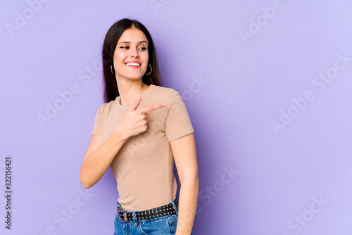 Young caucasian woman isolated on purple background looks aside smiling, cheerful and pleasant.