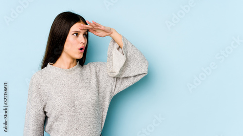 Young caucasian woman isolated on blue background looking far away keeping hand on forehead. © Asier