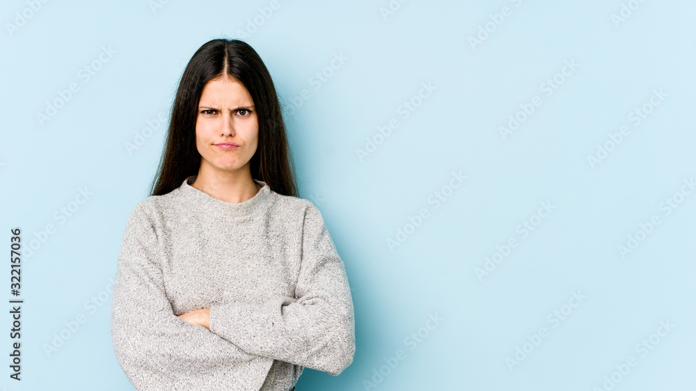 Young caucasian woman isolated on blue background frowning face in displeasure, keeps arms folded. Young caucasian woman isolated on blue background frowning face in displeasure, keeps arms folded.