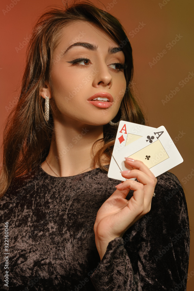 Brunette lady in black velvet dress and jewelry showing two aces, posing against colorful studio background. Gambling, poker, casino. Close-up. Brunette lady in black velvet dress and jewelry showing two aces, posing against colorful studio background. Gambling, poker, casino. Close-up.