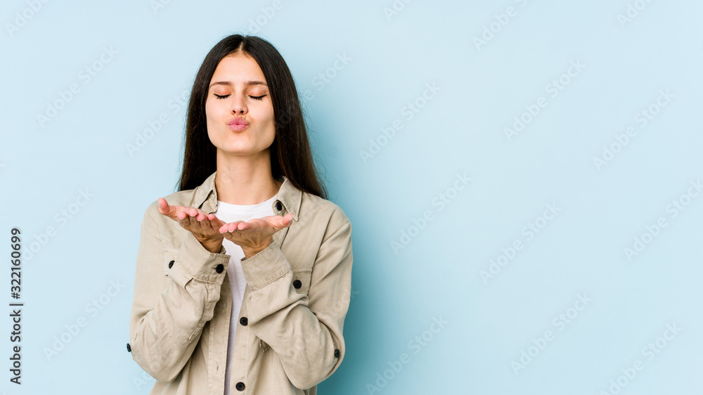 Young caucasian woman isolated on blue background folding lips and holding palms to send air kiss. Young caucasian woman isolated on blue background folding lips and holding palms to send air kiss.