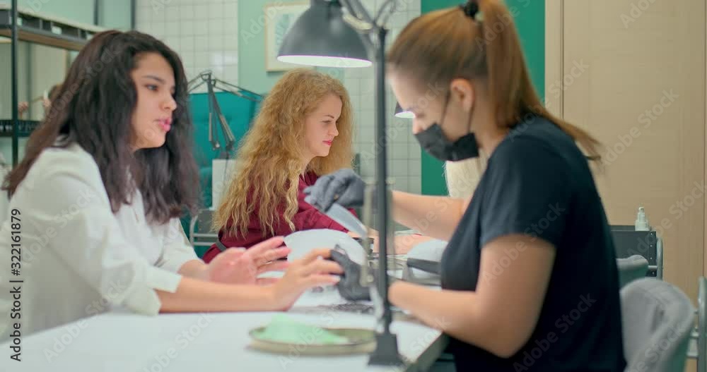 Beautiful girls are sitting on a manicure procedure in a modern manicure salon. Manicurists process nails to clients, workplace. Manicure salon with modern equipment. Beautiful girls are sitting on a manicure procedure in a modern manicure salon. Manicurists process nails to clients, workplace. Manicure salon with modern equipment.