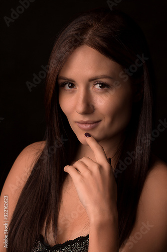 Portrait of a beautiful girl, long-haired brunette who looks at the camera and put her finger to the chin. Mysterious, pensive charismatic and seductive woman.