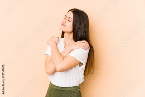 Young caucasian woman isolated on beige background hugs, smiling carefree and happy.