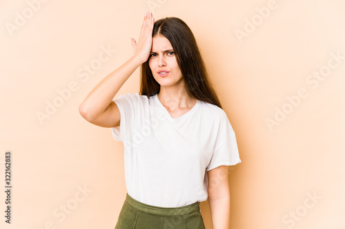 Young caucasian woman isolated on beige background forgetting something, slapping forehead with palm and closing eyes.